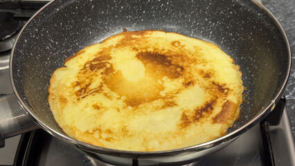 A homemade crêpe cooking in a non-stick frying pan
