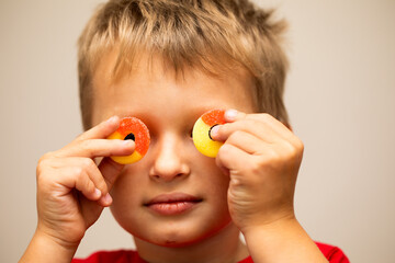 closeup a young boy covering his eyes with two peach ring gummies in his hands 