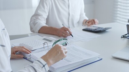 Team of accountants are working together, using a magnifying glass and a calculator, to audit financial reports in office. Audit and taxes in business