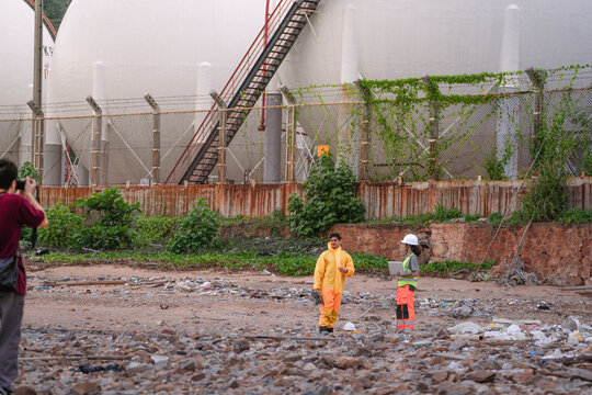 Two environmental specialists in safety gear conduct a field investigation at a polluted coastal site, collecting data and assessing contamination risks near an industrial zone.