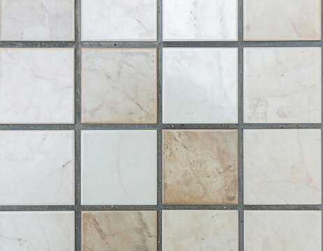 Close-up of a tiled surface with square, off-white and beige tiles and thin grey grout lines