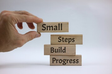 Hand Stacking Wooden Blocks Displaying 'Small Steps Build Progress' Message. isolated on white background