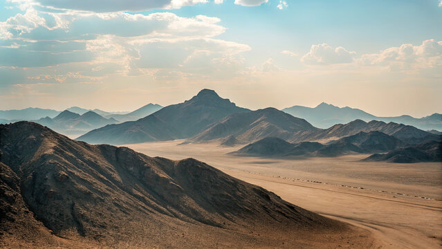 Long desert road with sandy mountain background concept. Breathtaking view of mountains under a vast, cloudy sky. - Powered by Adobe