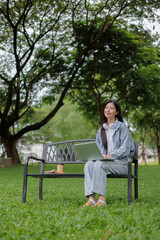 Fototapeta premium Young student working on laptop sitting on bench in park enjoying nature