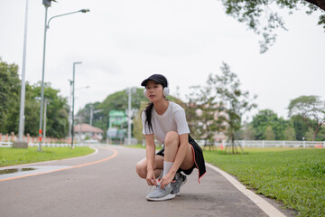 Young sportswoman tying shoelaces while listening music with headphones in the park