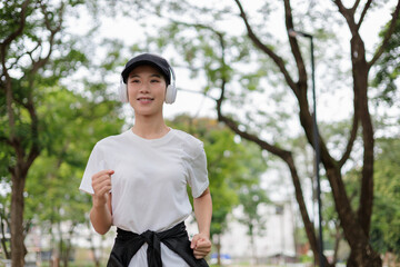 Fototapeta premium Young asian woman jogging and listening to music with headphones in a park