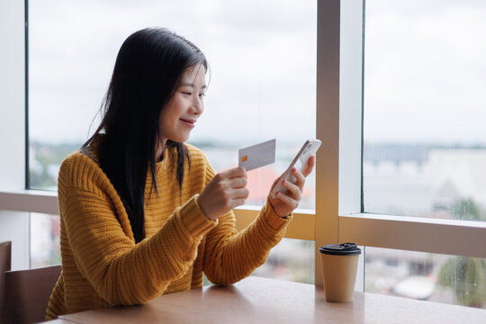 Young woman making online payment using credit card and smartphone in cafe