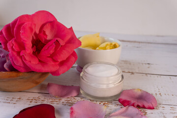 Close-up of a wooden table with red and yellow rose flower petals near a skin care cream.