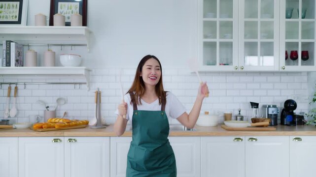 Young Asian woman dancing in the kitchen. The joy of a beautiful woman relaxing in her free time during the weekend in the house