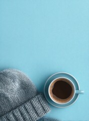 A grey knit beanie rests beside a cup of coffee on a light blue background; ample negative space