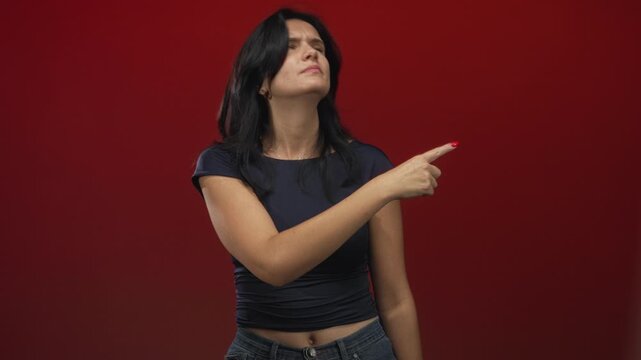 Young hispanic woman flicks finger dismissively in red studio with skeptical expression; defiance rejection.