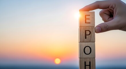 A hand carefully places a wooden block, spelling out the word "EPOCH" against a beautiful sunrise backdrop, highlighting the concept of new beginnings and the passage of time.