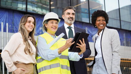 Architect using digital tablet with investors and businesswomen, discussing project details at construction site