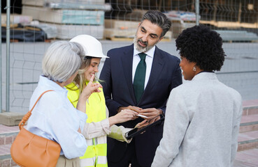 Multiethnic group of professionals collaborating on a construction project, using a tablet for blueprints and plans