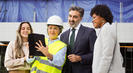 Diverse group of construction professionals collaborating on a project, using a digital tablet at a building site