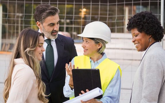 Female architect explaining building project to investors and managers using blueprint and tablet