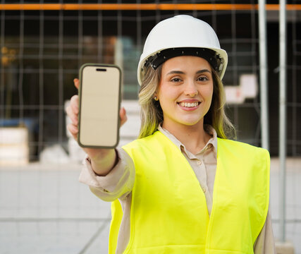 Young architect woman showing smartphone with blank screen at construction site