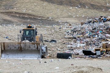 A large dump truck is driving through a pile of trash