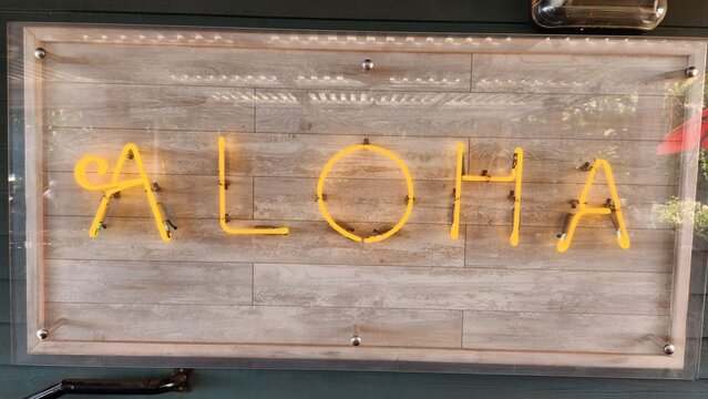 Aloha sign in yellow flourescent lights with wooden background, restaurant. Hawaiian vibes. 