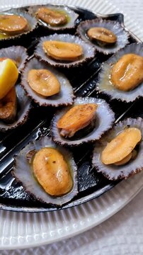 A close-up of a traditional Portuguese dish, grilled limpets (lapas).The dish is served in its own shell with a sauce of garlic, butter, and lemon.