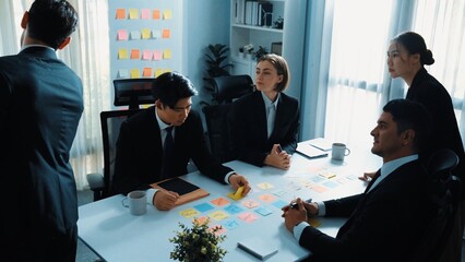Top view of smart businessman putting sticky note on whiteboard while marketing team brainstorm creative idea at meeting room. Leader explain startup project to group of diverse investor. Directorate.