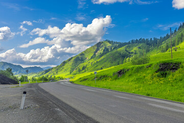 Majestic summer landscape with mountain road in Altai, Russia. Chuysky trakt road among green mountain valley above blue sky. Nature landscape in Altai Republic, Siberia, Russia