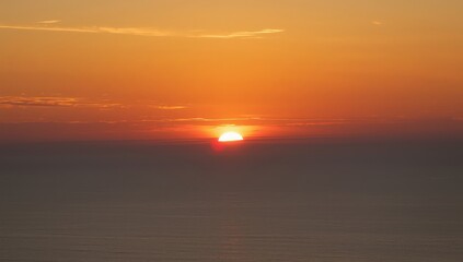 Obraz premium A bright sun setting over a hazy horizon with orange and yellow sky and dark water below it all