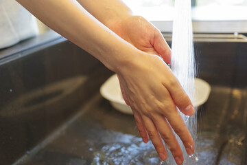 キッチンで手を洗う女性の手元（顔なし）