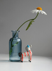 Minimalist still life with daisy flower in a stained glass vase and small toy horse.