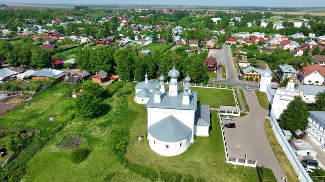 A drone's view of a beautiful white-washed Orthodox church surrounded by the traditional wooden houses and gardens of the historic town of Suzdal
