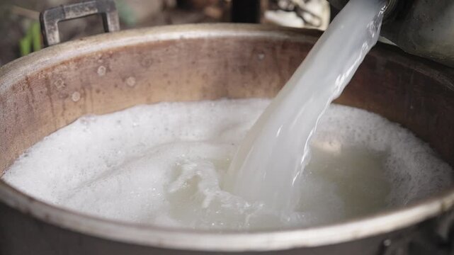 Close-up, pouring fermented sap from arenga pinnata tree in metal pot for distillation to produce arak or sopi alcohol in rural flores, indonesia, palm wine