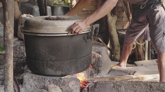 Farmer putting lid on metal pot on firewood, palm wine distillation, fermented sap from arenga pinnata tree, aren, for village liquor, arak, sopi, spirit