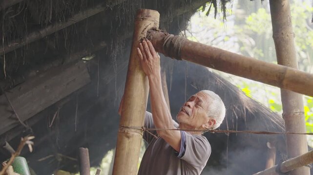 Old farmer sealing bamboo pipes in a traditional palm wine distillery in Flores, Indonesia, preparing equipment for distilling fermented sap into arak or sopi alcohol