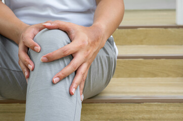 Morning run–related knee pain, person seated on wooden steps, hands gripping knee. Indicates...