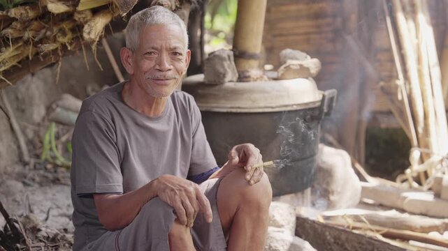 Portrait, indonesian palm wine farmer in flores, east nusa tenggara, indonesia, in local distillery on farm, fermented sap in metal cooking pot in background on a burning fireplace