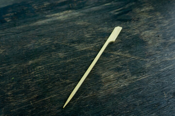 bamboo paddle pick isolated on wooden background.
These picks are ideal for serving appetizers, holding together sandwiches or wraps, and garnishing cocktails. Disposable bamboo barbecue skewer