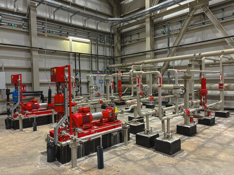 Industrial fire pump system inside a large facility, featuring bright red electric motors, beige pipelines, valves, and control systems. It emphasizes safety, engineering, and industrial maintenance.