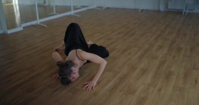 Girl in black suit moves on floor and performs contemporary parter choreography during her graceful theatrical dance moves in studio
