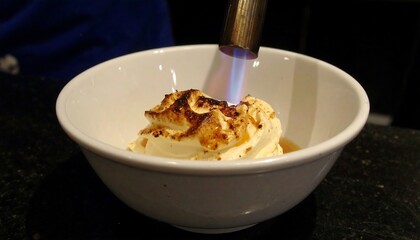 A creamy dessert is being flamb?ed with a kitchen torch, showcasing a caramelized, golden-brown topping.