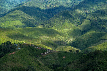 many cabin huts of a small village on the one of slope of complex mountain in sun shine and shade of clouds