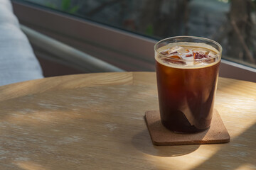 a glass of iced americano coffee on wooden table in sun light and shade