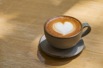 latte coffee art on wooden plate at desk in sun shine with shade of the tree