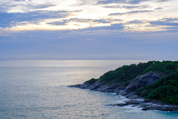 landscape scene of rock shore of one conner edge of a small island in a deep blue sea in cloudy blue sky