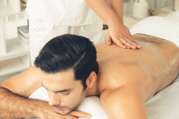 Caucasian man customer enjoying relaxing anti-stress spa massage and pampering with beauty skin recreation leisure in day light ambient salon spa at luxury resort or hotel. Quiescent