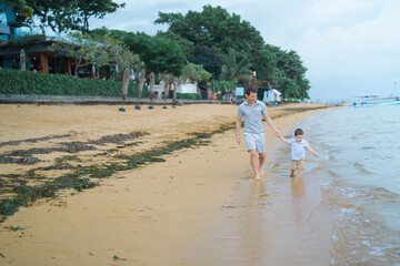 Father and young toddler son walk and play in the sand on the beach in Bali, Indonesia