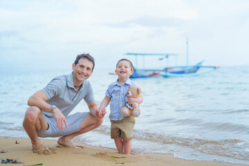 Fototapeta premium Father and young toddler son walk and play in the sand on the beach in Bali, Indonesia