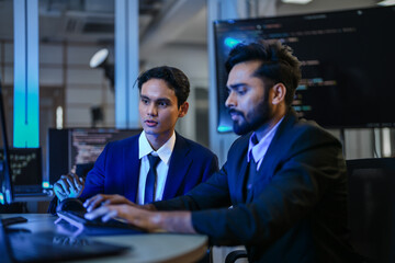 diverse AI developers collaborate in a late-night coding session. A senior engineer mentors his colleague as they program a complex machine learning algorithm together.