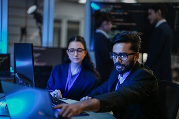 A diverse team of AI developers shares a successful moment in the office. A female programmer smiles as they review the positive results of a complex machine learning algorithm.