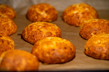 Freshly baked cheese buns cooling on parchment paper. The buns have a golden-brown crust,...