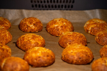Freshly baked cheese buns cooling on parchment paper. The buns have a golden-brown crust, indicating perfect baking. Ideal for illustrating homemade baking or culinary delights.
